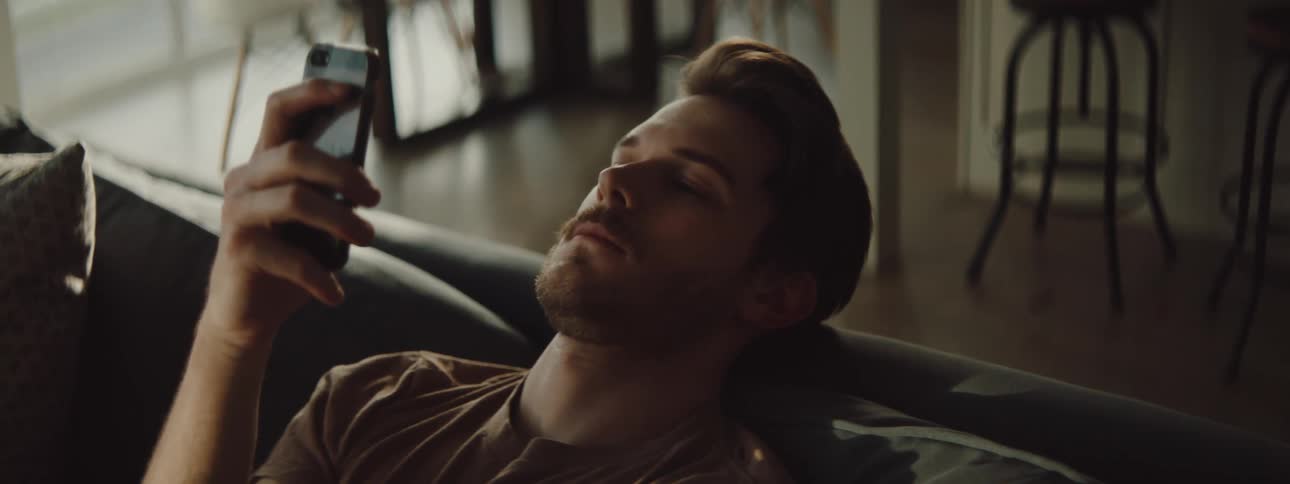 Man sitting on couch leans back viewing mobile phone