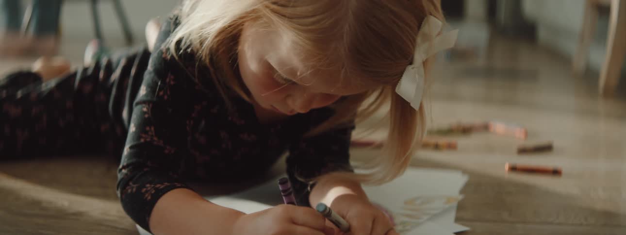 A young girl lies on the floor at home and colors