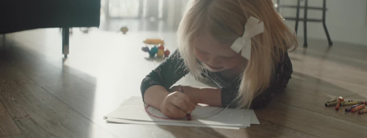 A little girl lies on the floor at home and colors