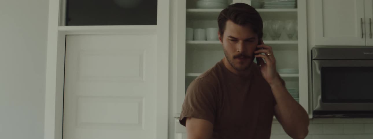 A man looking tense is pacing in the kitchen while eating and having a cell phone to his ear