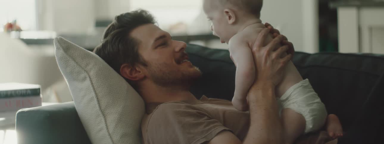 A man lifts a baby up while laying on the couch