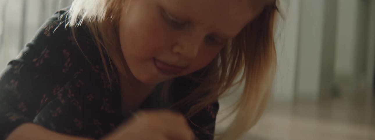 A toddler girl laying on the floor using a crayon to color