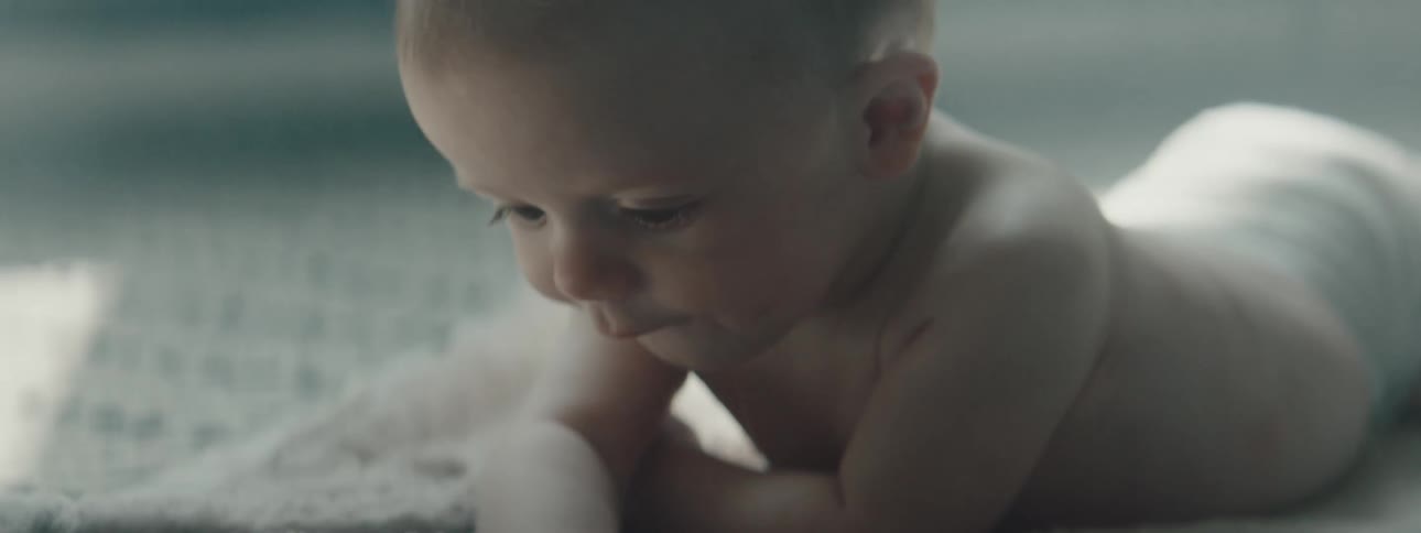 A baby wearing a diaper is laying on a blanket and moving around and playing