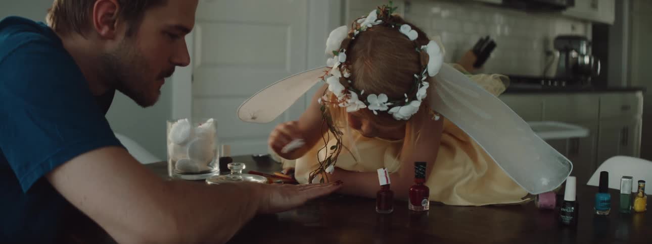 A girl on a table putting nail polish on a mans hand with a wall in the background