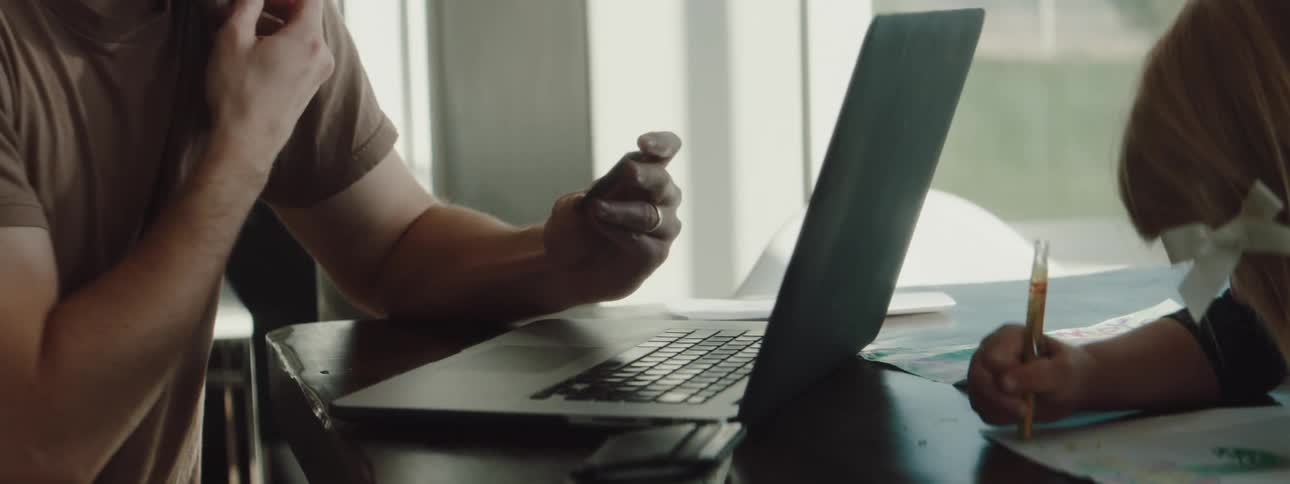 Girl draws on paper as father uses mobile phone and types credit number on laptop before putting credit card back into wallet