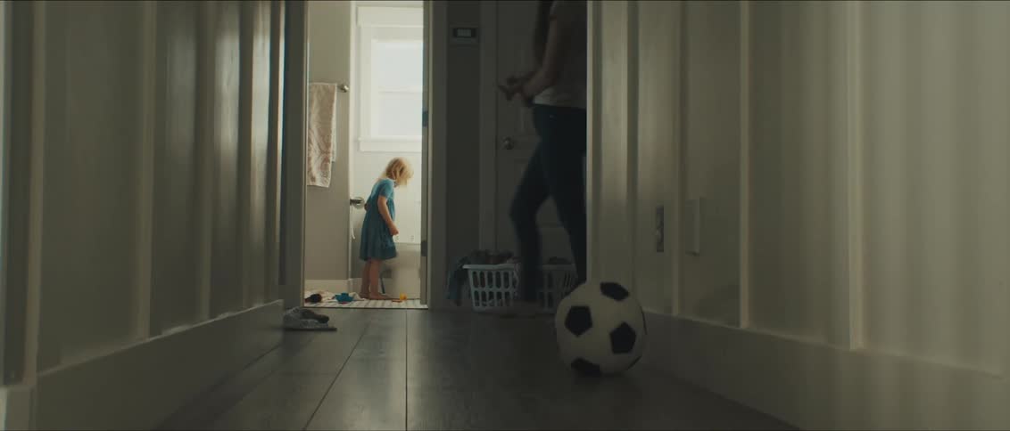 A young girl stands in the bathroom and a woman walks in the hallway beside her