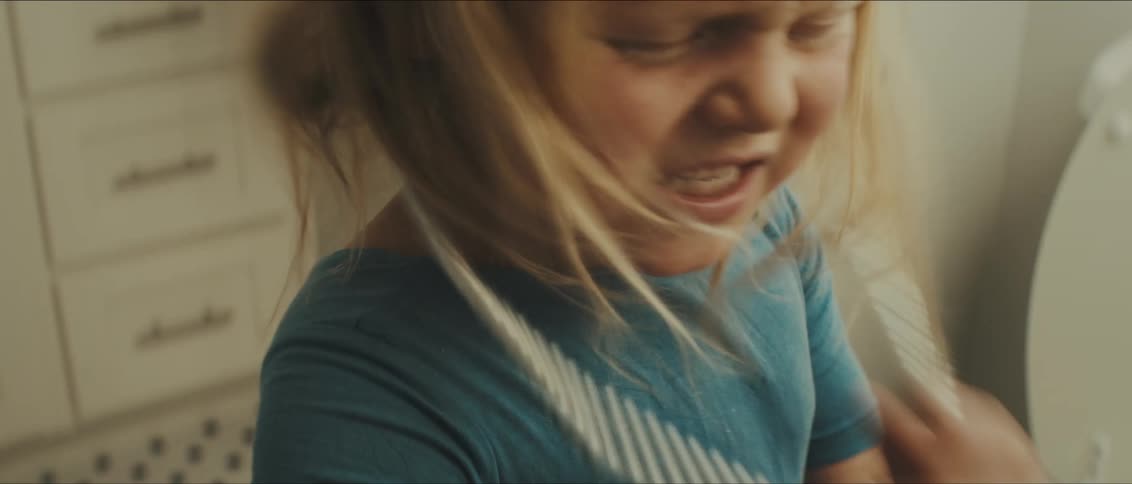 A child is standing indoors and breaks a necklace in half