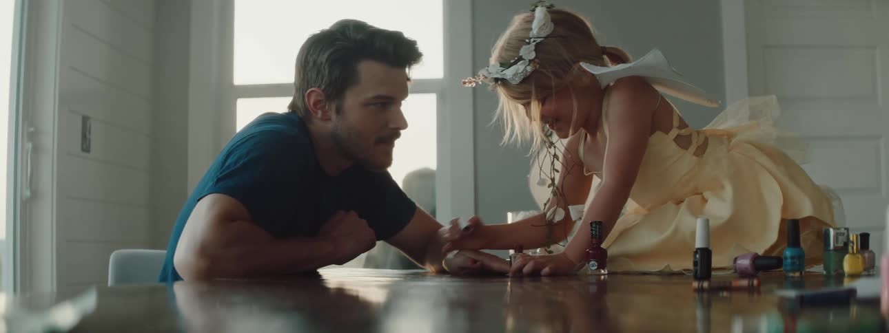 A young girl sits on top of a counter painting her fathers fingernails with nail polish