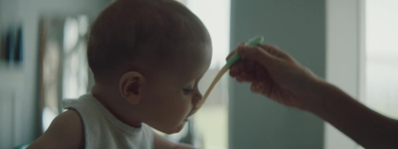 A baby wearing a bib chews and takes more food from a spoon
