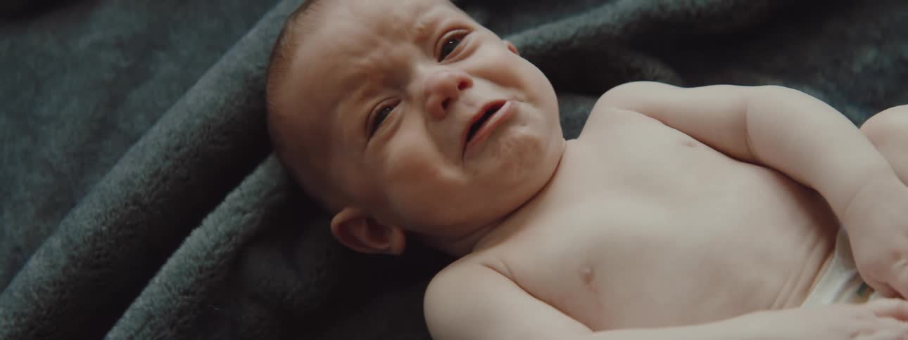 A baby laying down on blankets is crying