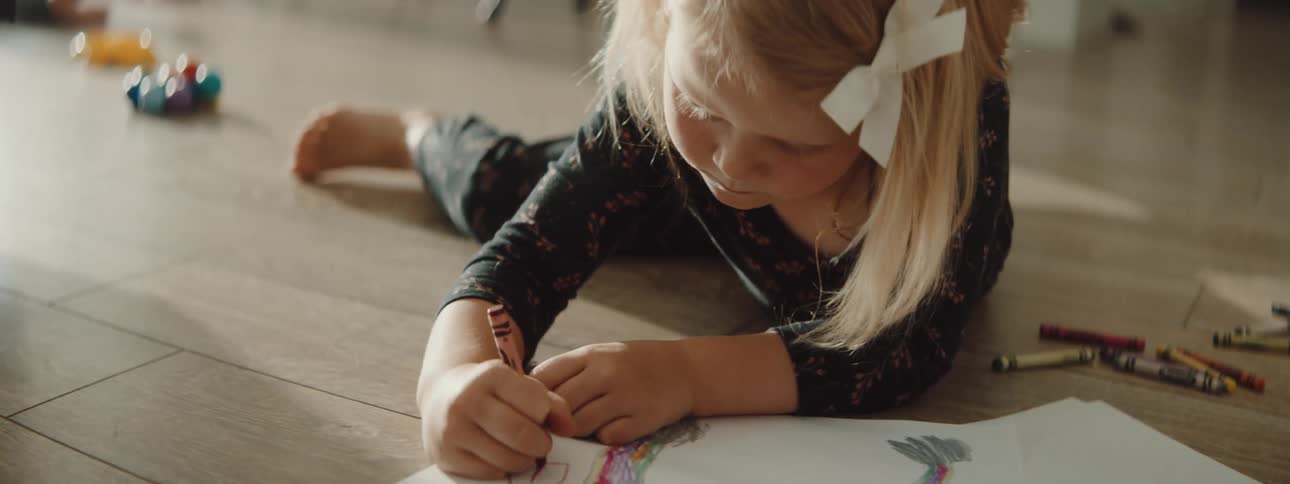 A child is drawing pictures with color crayons indoors