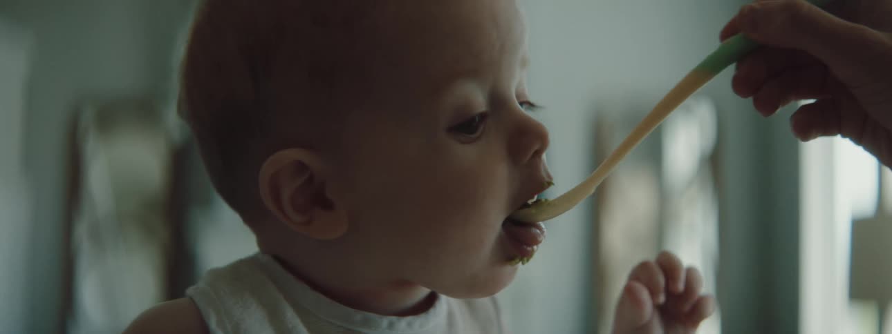 An adult feeds a baby with a baby spoon indoors during the day