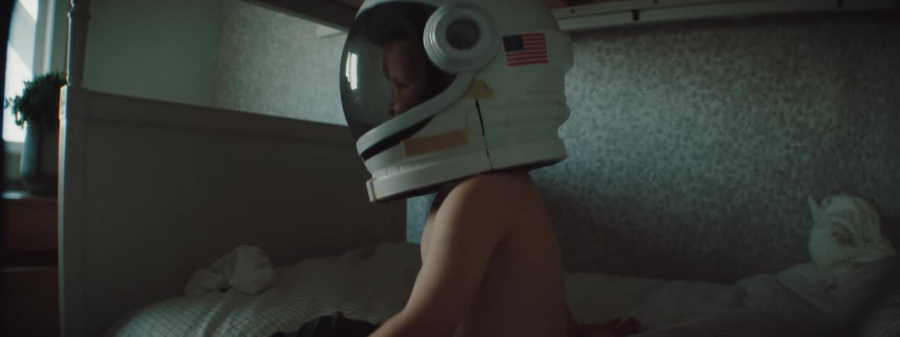 A young boy sits in his bed with a space helmet on
