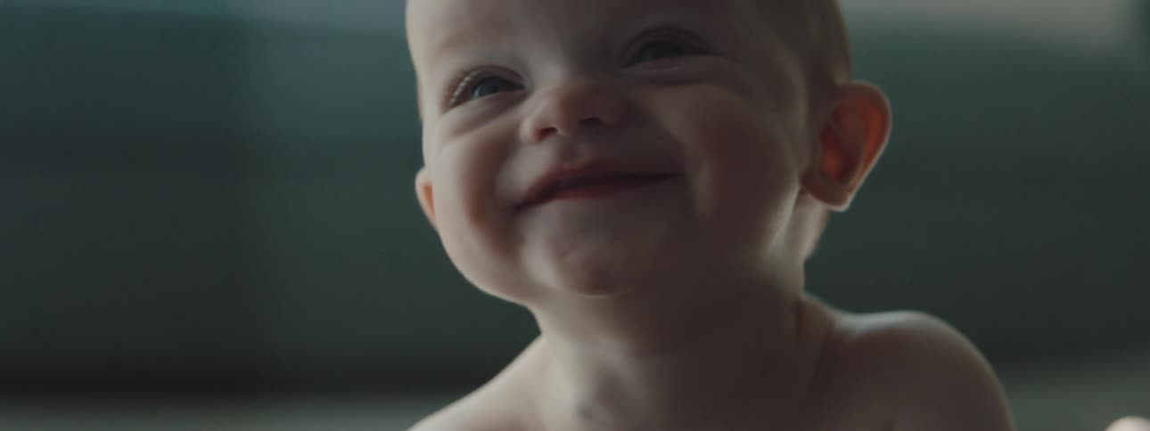 A baby lying down on the floor lifts his head and smiles