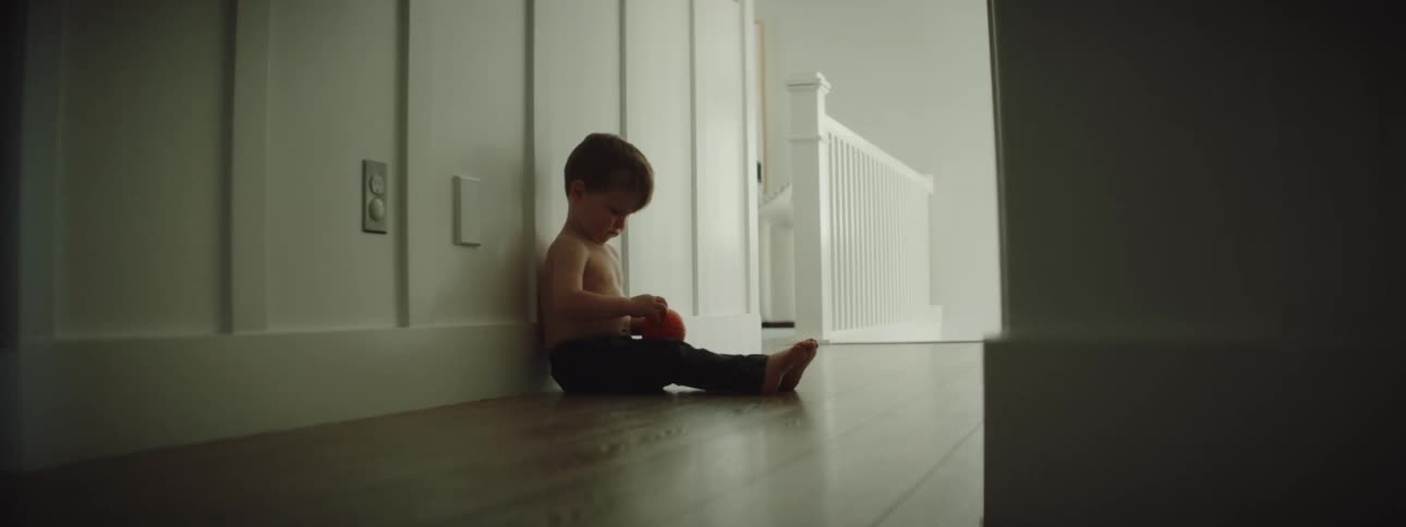 Toddler sitting in the floor on a hallway at home playing with a red ball
