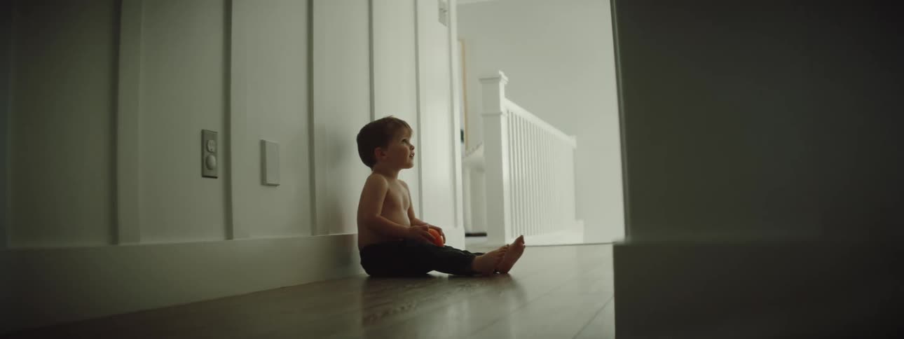 Shirtless toddler boy holding a toy sits on the floor