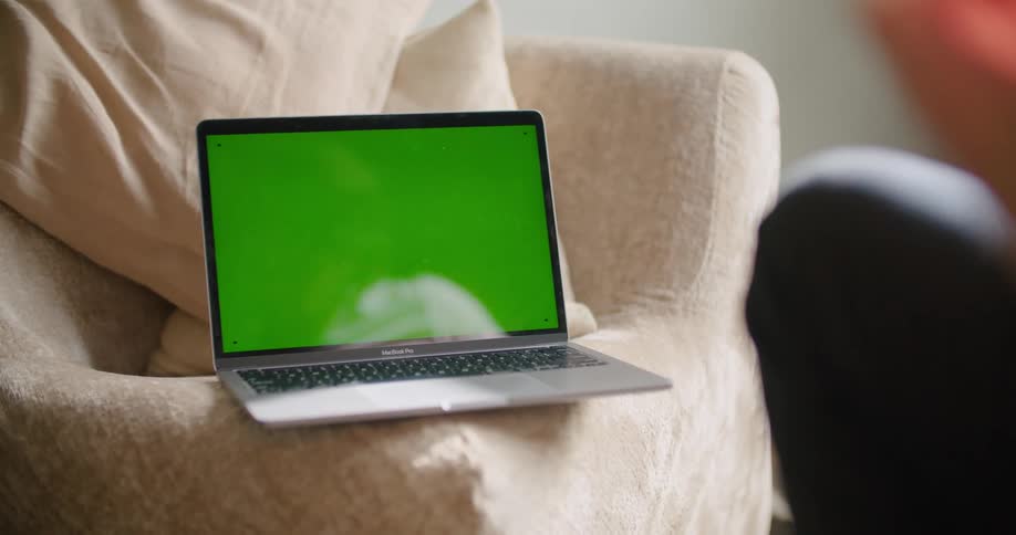 Laptop with green screen on sofa with cushions on