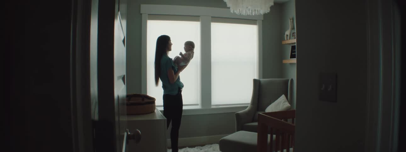 Mother with a blue shirt and black pants holding baby is silhouetted against the windows