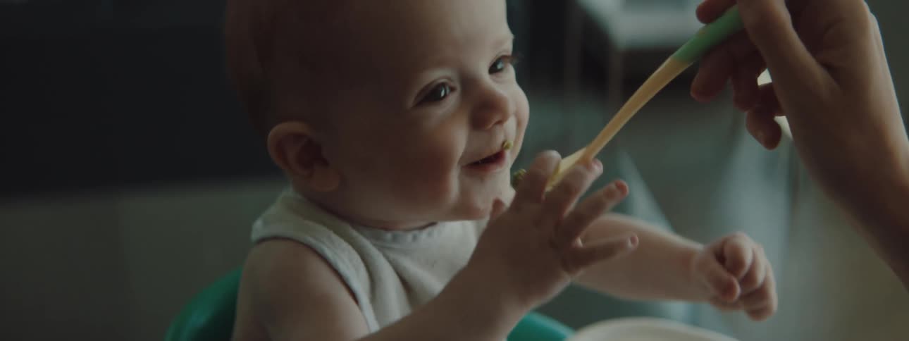 A parent is feeding their infant food indoors