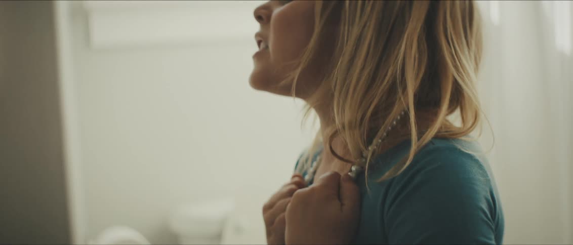 A young girl stands in the bathroom and tries to yank off a pearl necklace