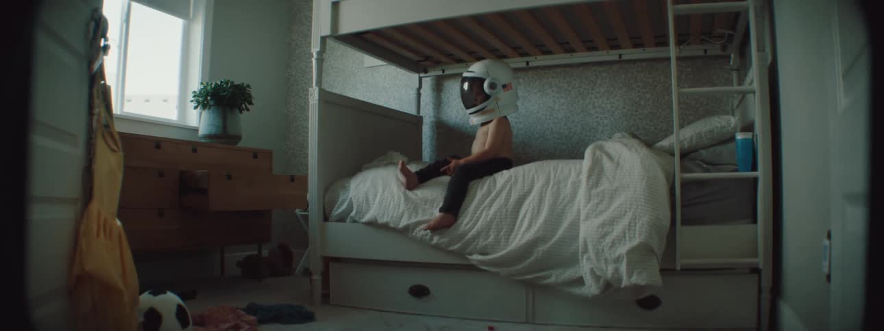 A small child sitting on a bed wearing a helmet playing