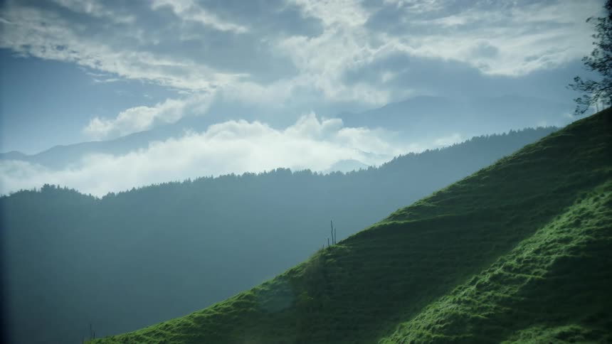 Grass covered hillside with mountains in the distance under a cloudy sky