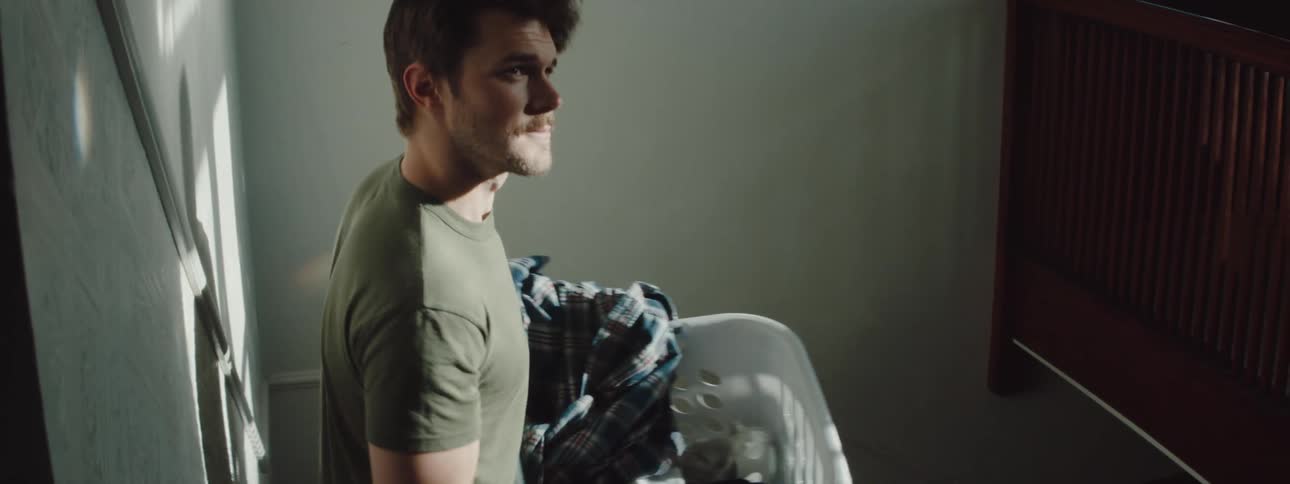 A man with a laundry basket walking down a staircase with a banister with a wall in the background