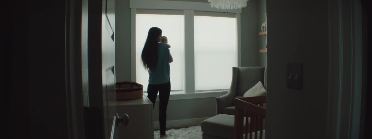Mother with a blue shirt and black pants holding baby is silhouetted against the windows