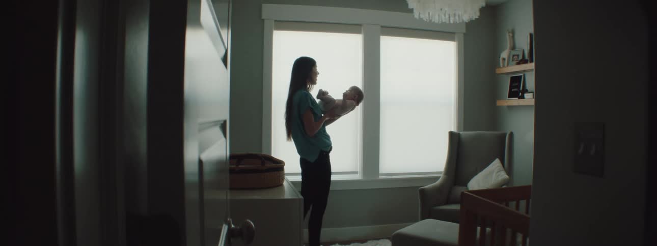 Mother with long straight hair and a blue shirt holds her baby and talks to him in the baby room