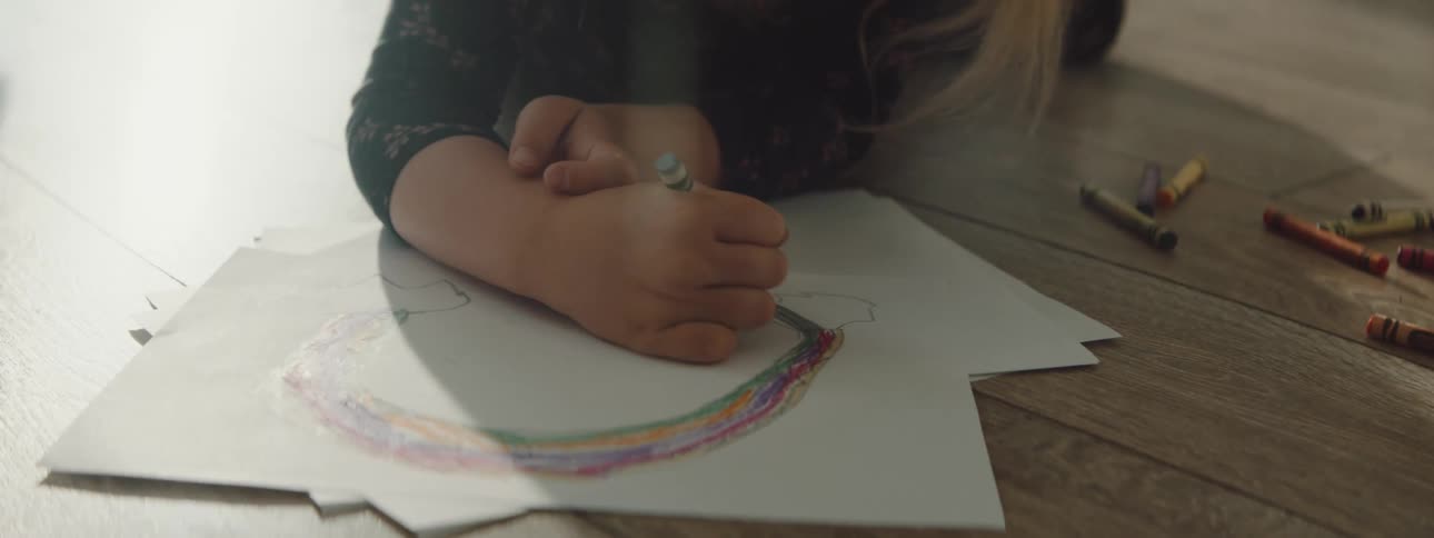 A child is coloring on paper on the floor
