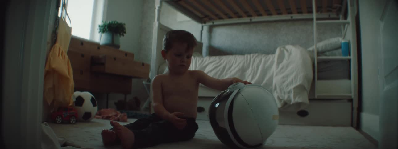 A child in a room playing with a helmet with a bed a wall and a window in the background