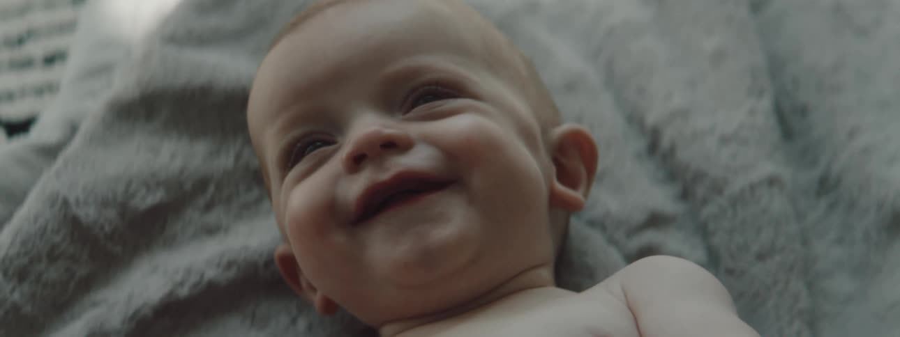 A baby is laying on a blanket moving its arms around and smiling