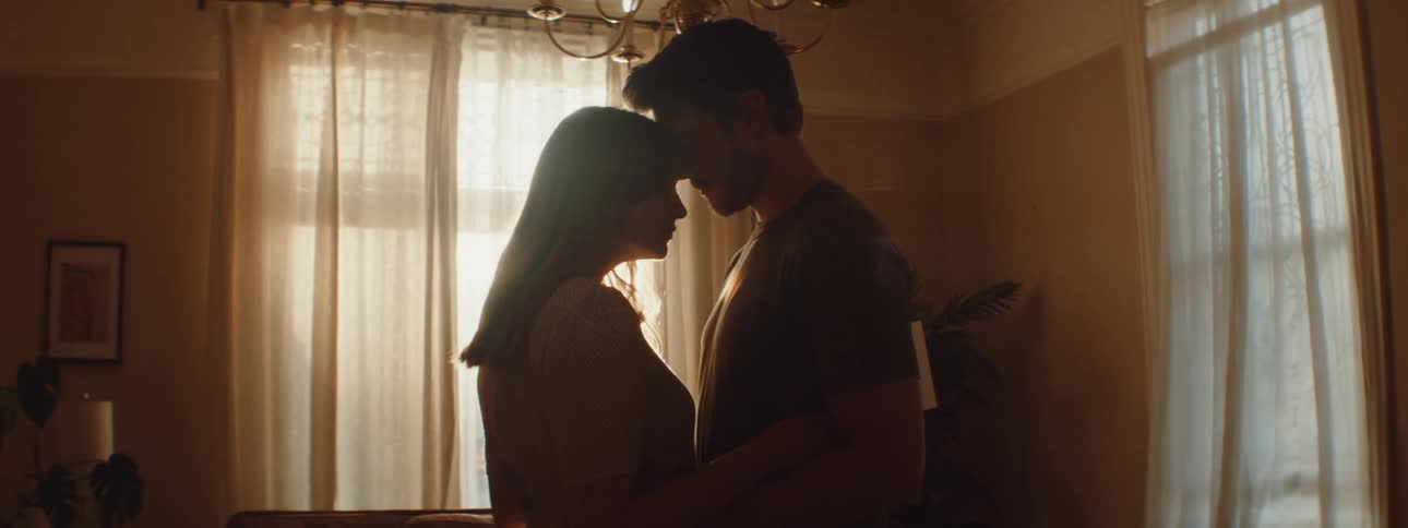 Morning sunlight filters between a couple hugging and kissing in the living room