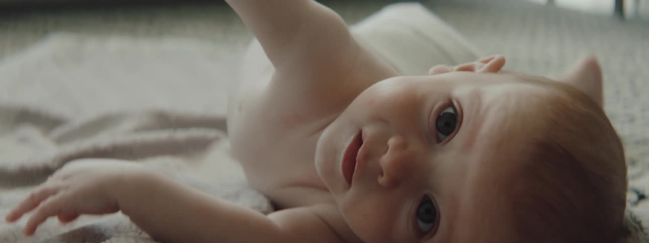 Baby lying on rug reaches hand out then rolls onto side