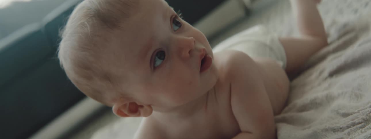Baby rolls over to lie on stomach on carpet near couch while looking around