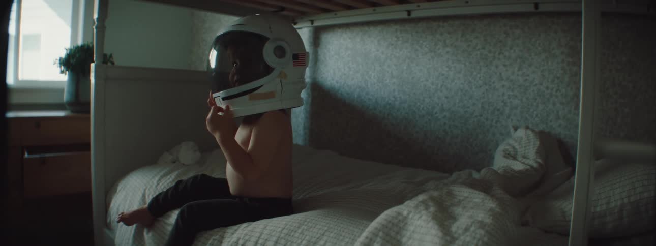 Boy sitting in a bed at home playing with an astronaut helmet