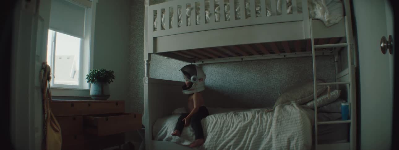 A child sitting on a bed wearing a space helmet
