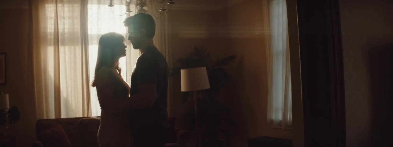 A man and woman hug in the dark living room