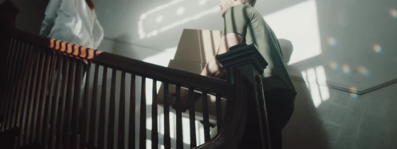 A man and woman carry boxes and a laundry basket up a home staircase