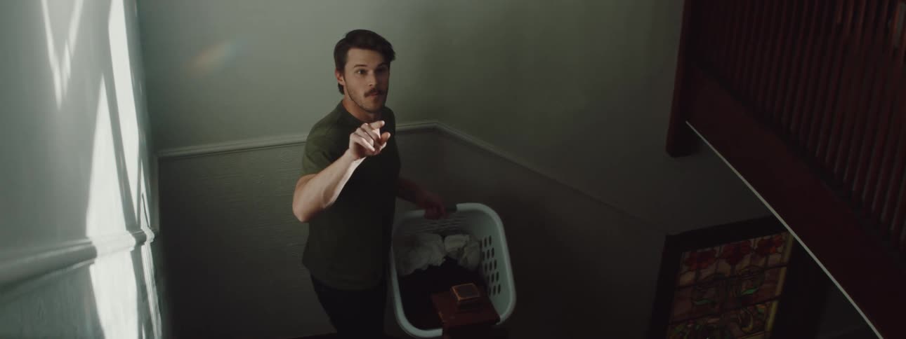 Man walking down the stairs with laundry playfully throws clothes to her wife