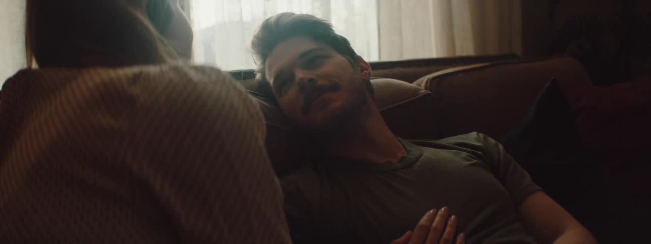 A man and a woman in a room on a couch with a wall and window in the background