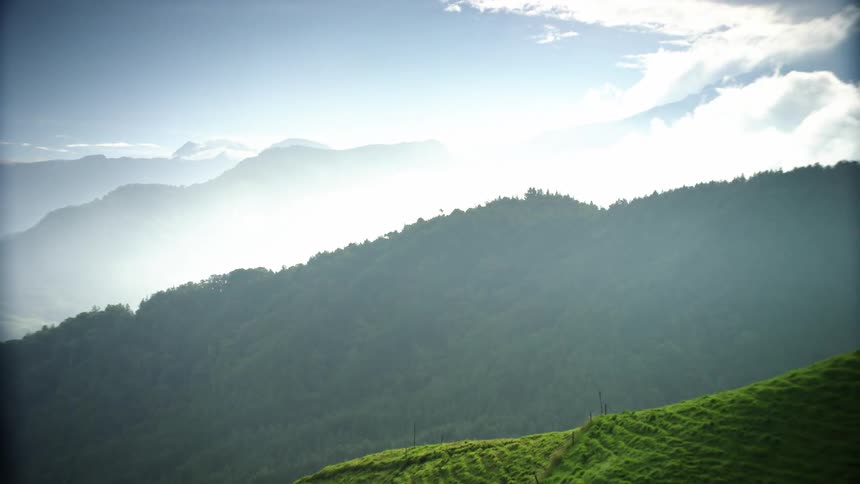 Grass covered hills with mountains in the distance under a foggy cloudy sky