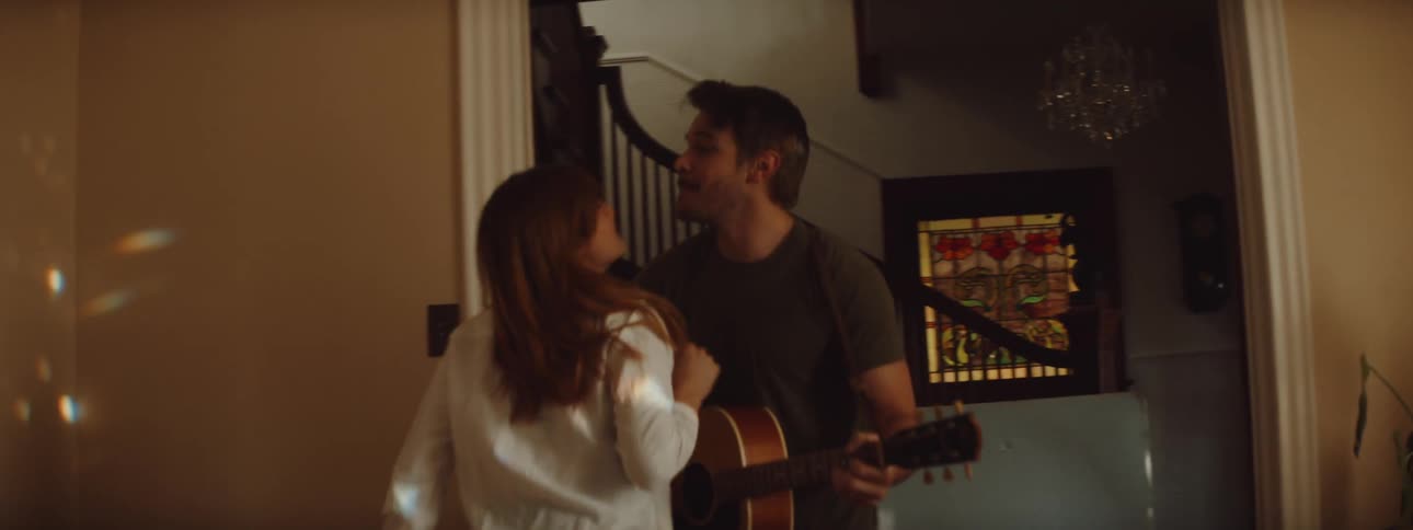Man playing acoustig guitar in a room at home dancing with his wife