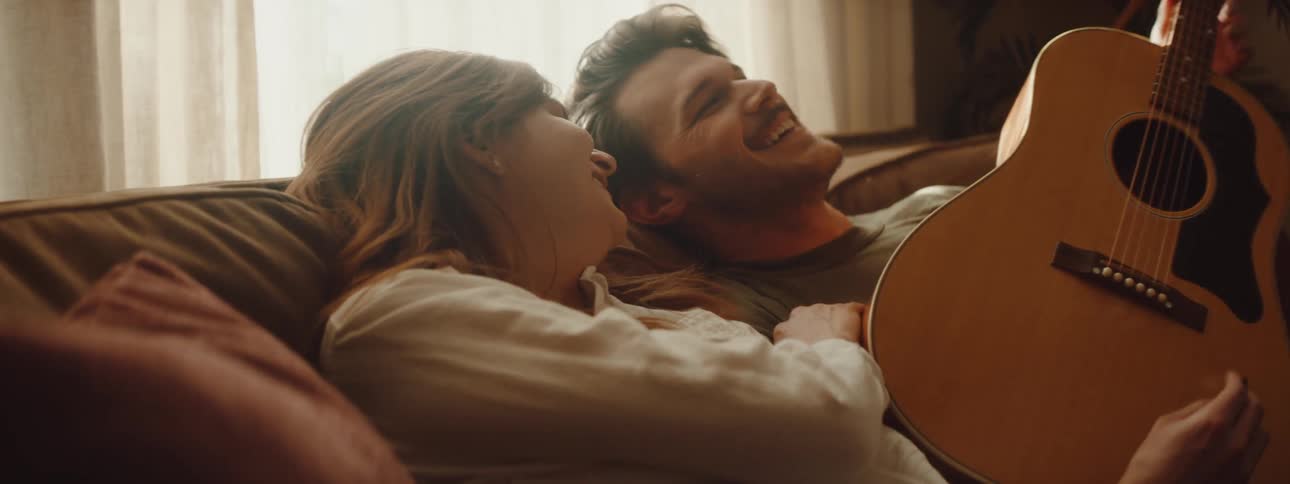 A man is holding a guitar as he sits with a woman