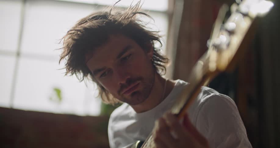 A man is sitting indoors and playing a guitar