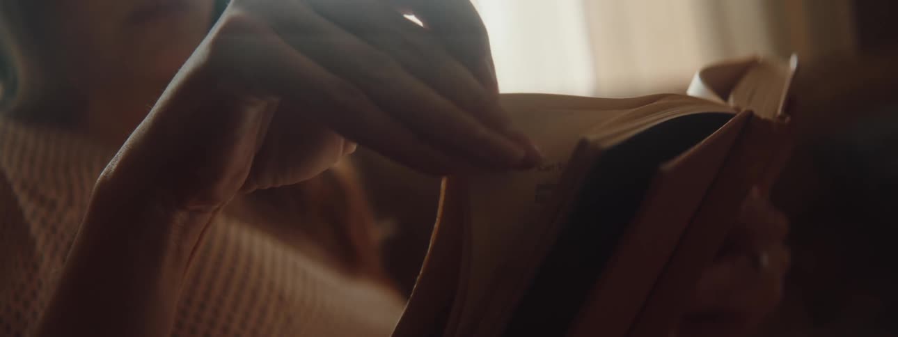 A woman is sitting indoors and reading a book