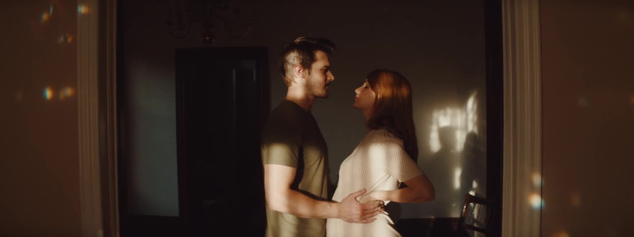 Young pregnant couple kissing on a dimly lit room at home