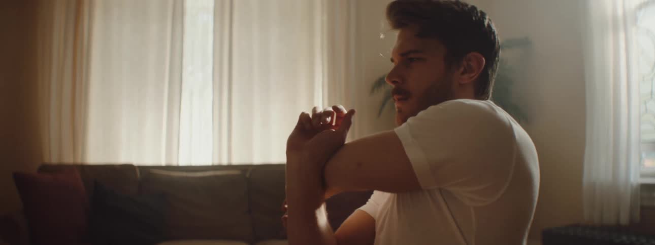 A man stretches one arm and shoulder then the other in his living room on a sunny day