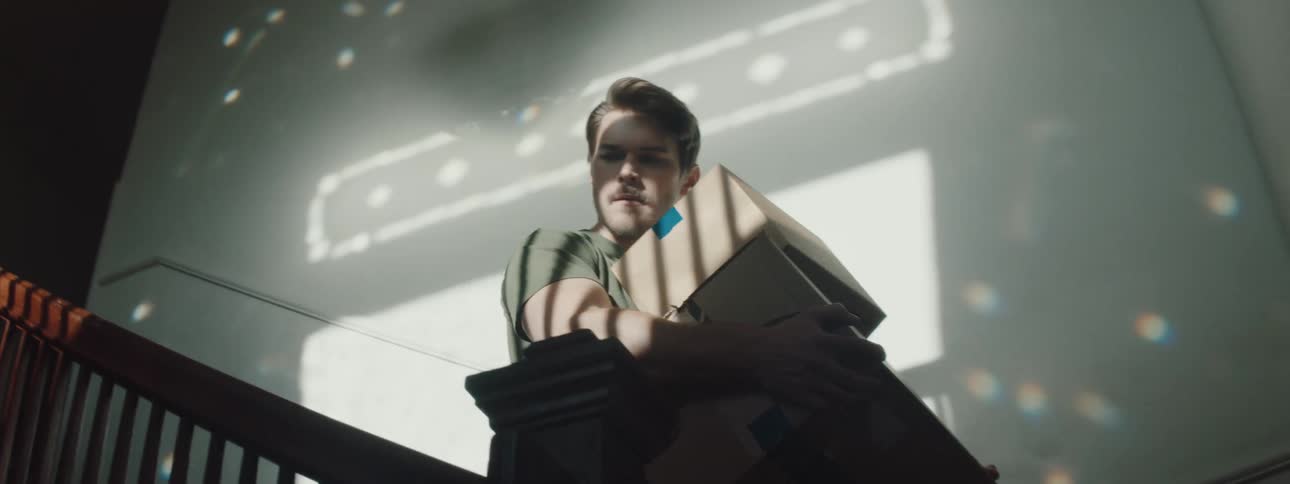 Man with a beard and t shirt carries boxes and goes downstairs