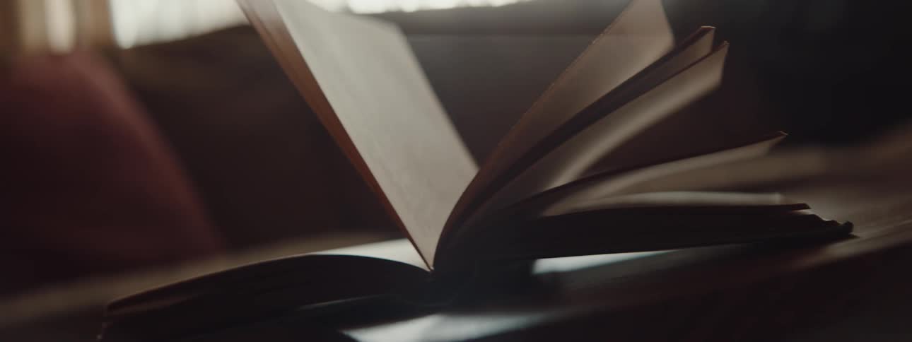 Pages of an open book over a table swinging with the breeze inside a room